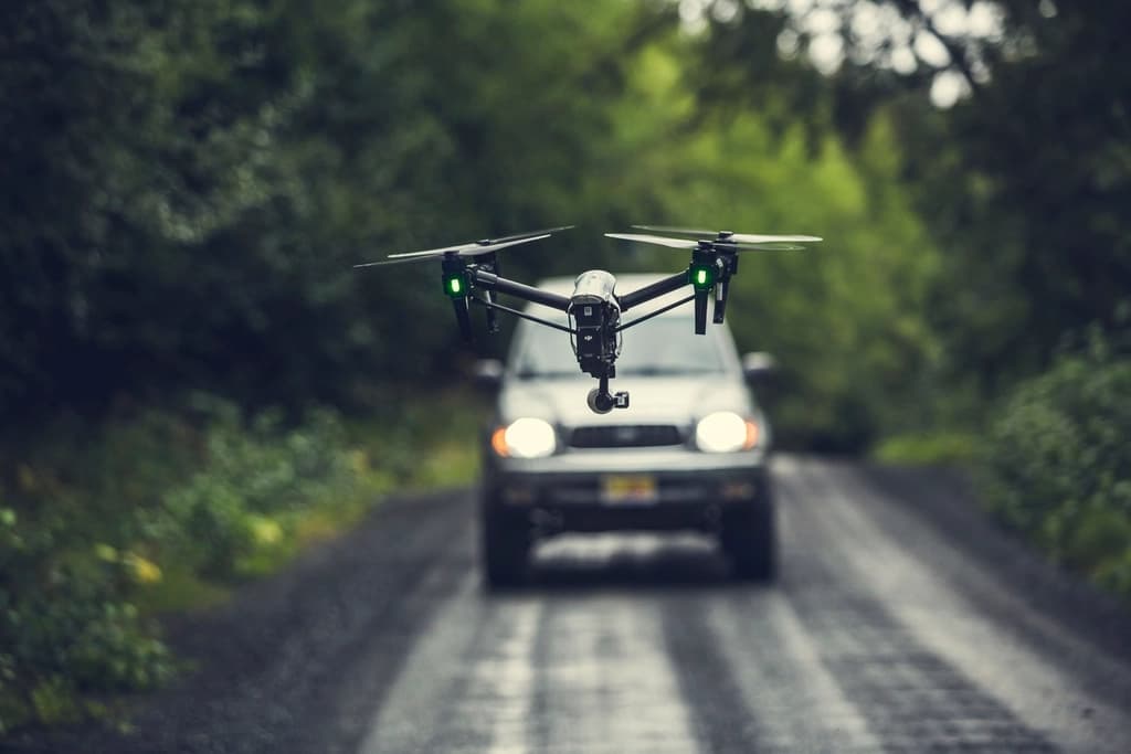 A quadcopter drone in flight above a forest road.
